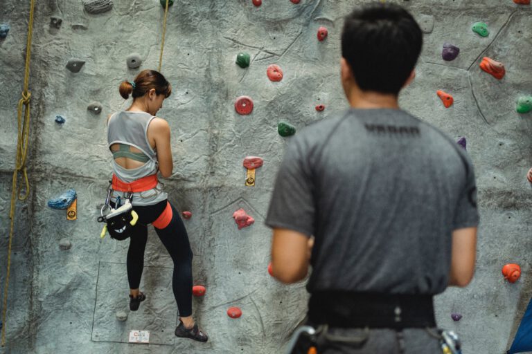 Eine Frau hängt am Seil vor einer Kletterwand. Daneben steht ein Mann.