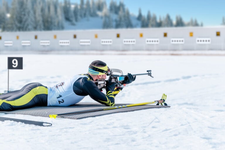 Ein Biathlet zielt liegend auf eine Zielscheibe