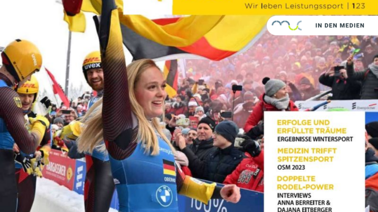 Eine lachende Rodlerin schwenkt eine Deutschlandfahne vor Publikum.